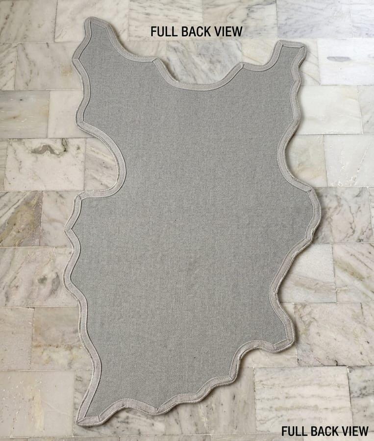 Detailed-3d-hand-carved-high-low-pile-texture-new-zealand-wool-pink-sakura-flower-rug A gray fabric rug or mat with an irregular, wavy outline is laid flat on a light beige marble tile floor. Text overlays read 'FULL BACK VIEW' at the top and 'FULL BACK VIEW' at the bottom right.