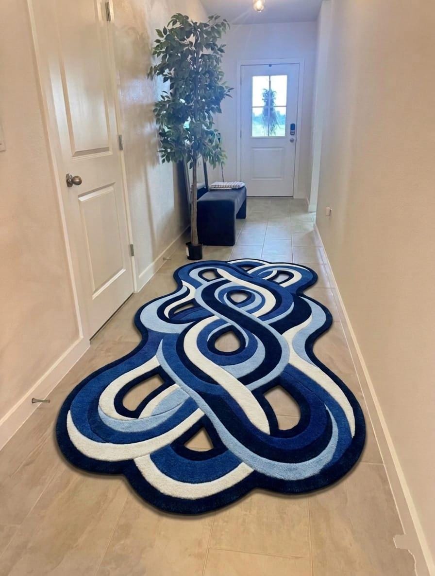 Shubham-Art-Rugs-hand-tufted-abstract-wavy-wool-rug-irregular-blue-area-carpet A blue and white abstract knot-patterned area rug placed on a light wood hallway floor, with white walls, doors, a potted plant, and a small bench in the background.