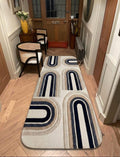 Shubham-Art-Rugs-hand-tufted-new-zealand-wool-arch-rug-navy-blue-beige-ivory-contemporary-carpet A long rectangular area rug with a mid-century modern geometric arch pattern in navy blue, beige, and cream, shown on a light wood herringbone floor in a hallway.