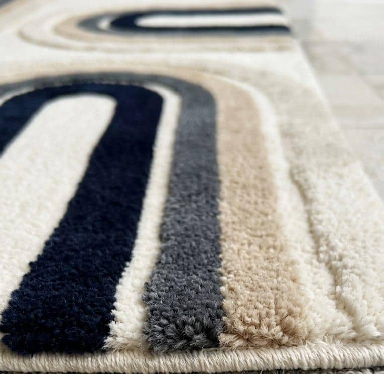 Detailed-hand-carved-high-low-pile-texture-geometric-archway-navy-blue-wool-rug  Close-up of a plush shag rug with a modern abstract design featuring thick vertical stripes in navy blue, charcoal gray, and cream on a light beige base.