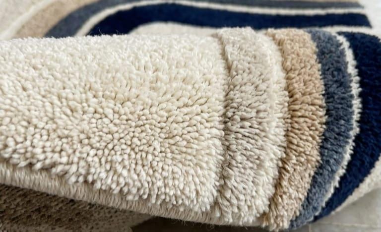 Detailed-hand-carved-high-low-pile-texture-geometric-archway-navy-blue-wool-rug Close-up of a plush, high-pile terry cloth or fleece fabric in cream, beige, and navy blue stripes.