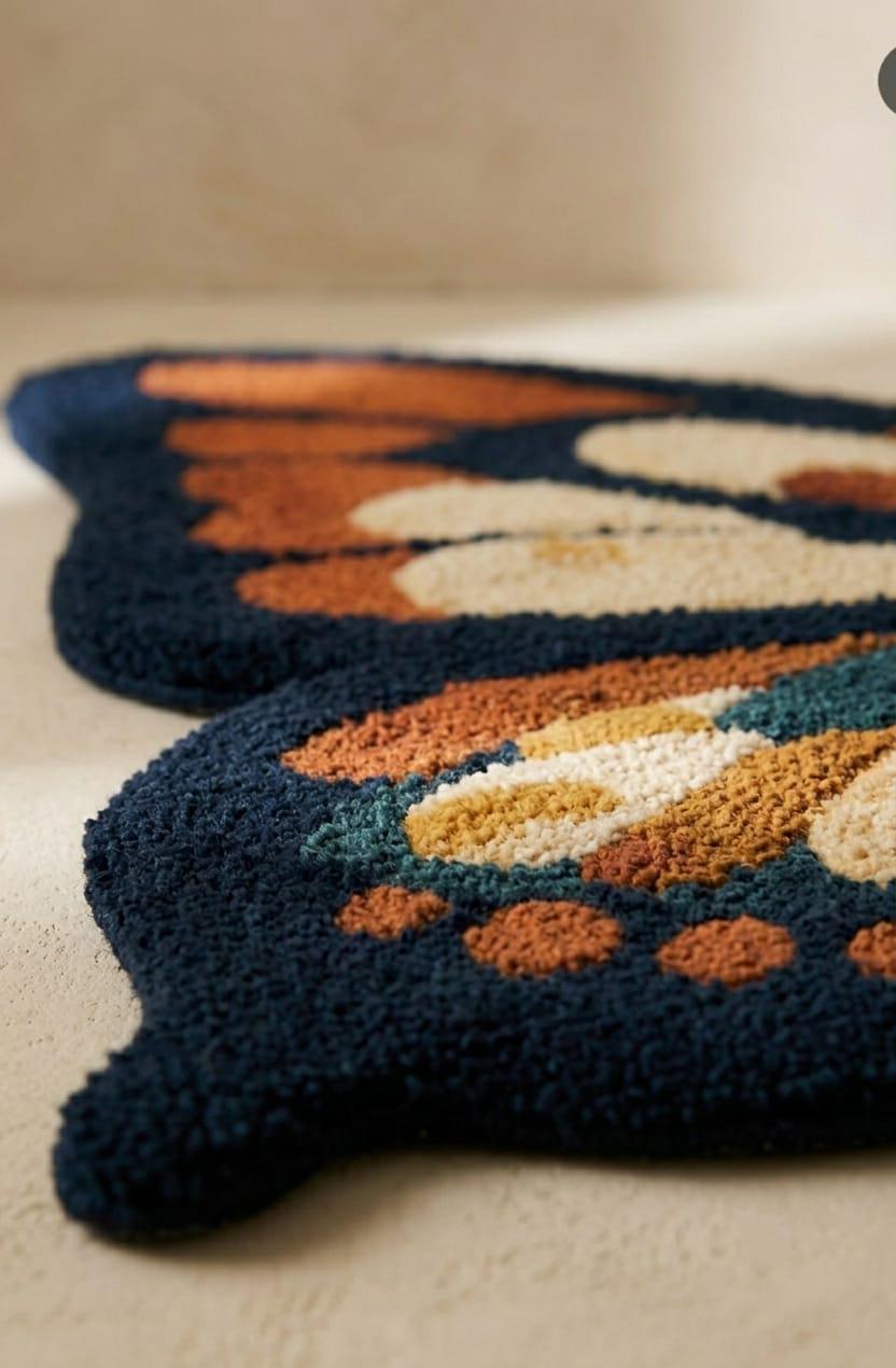 Detailed-3d-hand-carved-high-low-pile-texture-new-zealand-wool-pink-and-rust-butterfly-wing-rug
A close-up of a textured, tufted rug with a butterfly design, featuring a dark navy blue base with orange, cream, and teal accents, resting on a light beige floor.