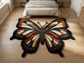  Shubham-Art-Rugs-hand-tufted-new-zealand-wool-butterfly-rug-boho-nursery-floor-art A large butterfly-shaped area rug with orange, cream, and black patterned wings, placed on a light wood floor in a bedroom with a bed visible in the background.