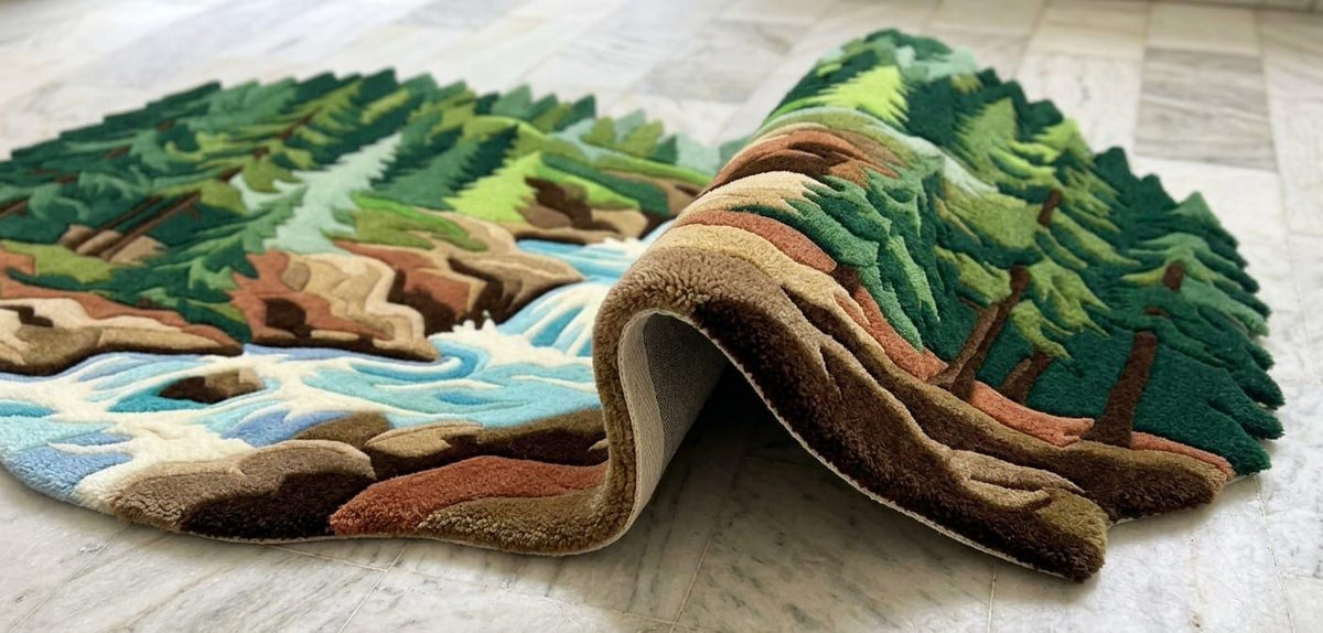Detailed-hand-carved-multi-level-high-low-pile-texture-new-zealand-wool-scenic-woodland-rug  A 3D layered area rug shaped like a forest landscape with a waterfall, shown partially rolled up on a light-colored tile floor.