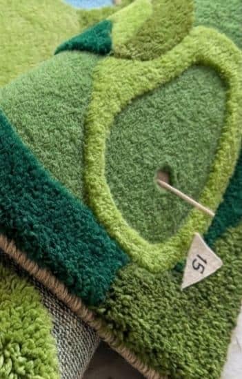 Detailed-3d-topography-hand-carved-high-low-pile-texture-sports-green-golf-rug A close-up of a green textured rug with a raised leaf-like pattern, showing a small white size tag marked '15' on the product.