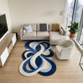 Shubham-Art-Rugs-hand-tufted-new-zealand-wool-rug-blue-abstract-organic-modern-area-carpet A modern living room featuring a large abstract looped area rug in shades of navy, blue, and cream on light wood floors. The room is styled with a beige sectional sofa, a white accent chair, a media console, and a large window overlooking a city skyline.