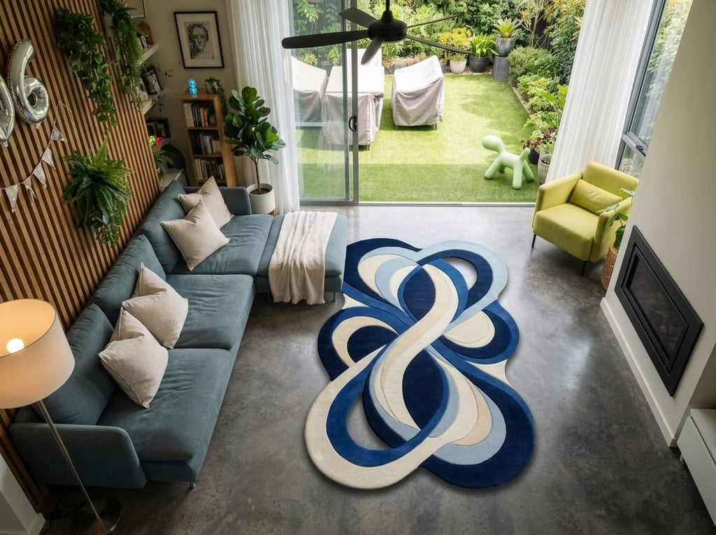 Shubham-Art-Rugs-hand-tufted-new-zealand-wool-rug-blue-abstract-organic-modern-area-carpet A modern living room featuring a prominent round area rug with an abstract blue, navy, and cream infinity loop pattern on a concrete floor. The room is styled with a slate blue sectional sofa, a green accent chair, and a large window looking out to a green backyard.