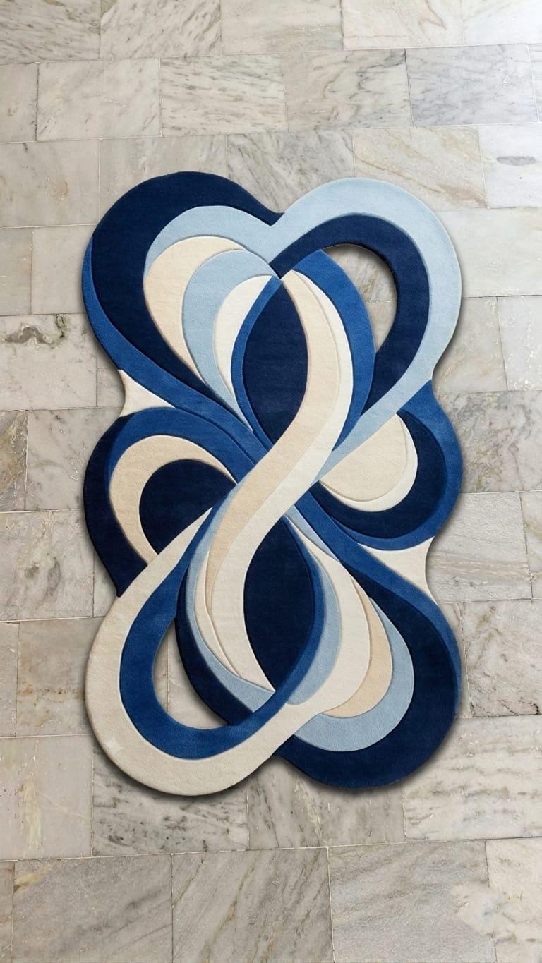 Modern-contemporary-living-room-interior-styling-featuring-luxury-fluid-blue-abstract-organic-area-carpet An abstract, layered oval rug with interlocking loops in navy blue, medium blue, light blue, and cream, displayed on a light beige marble tile floor.
