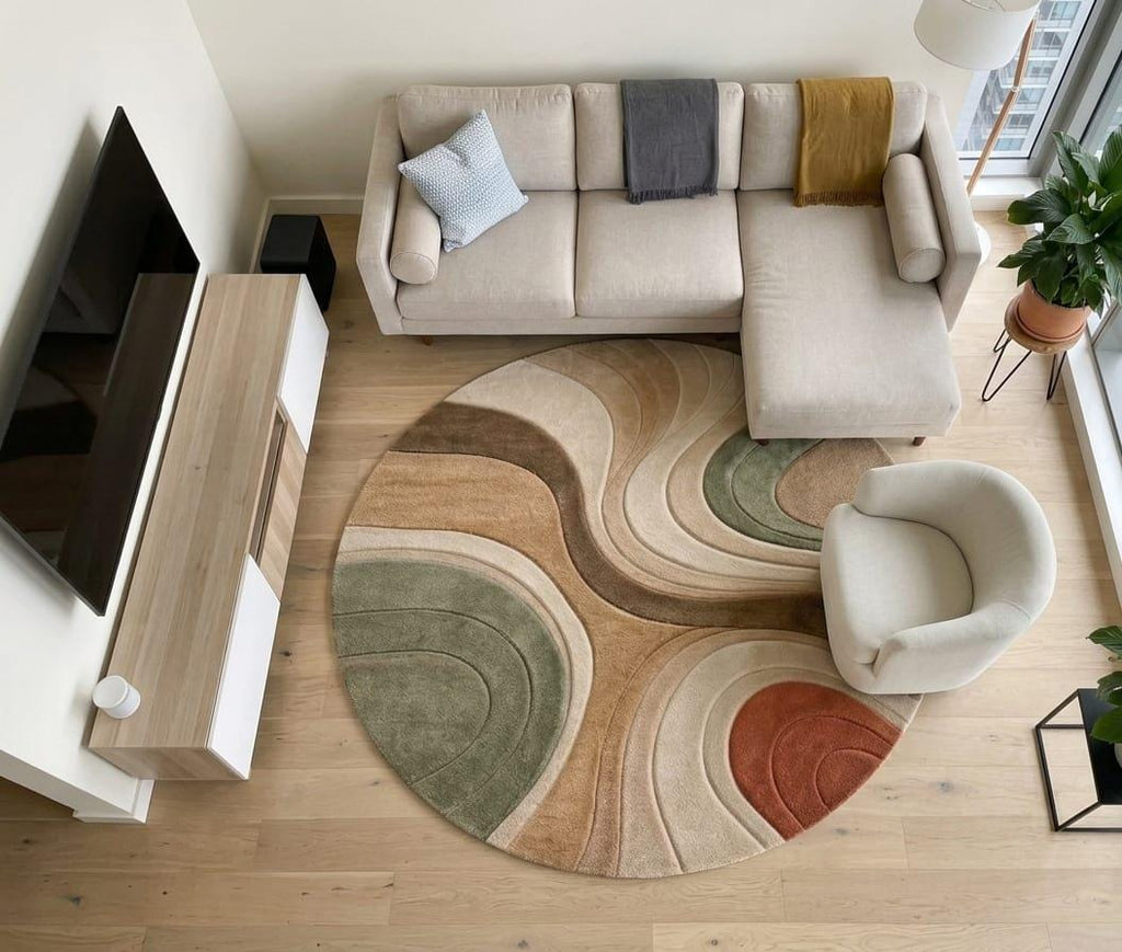 Shubham-Art-Rugs-hand-tufted-wool-area-rug-abstract-wavy-sage-green-terracotta-beige-contemporary-home-carpet A round area rug with an abstract wavy pattern in beige, brown, sage green, and terracotta, styled in a modern living room with a beige sectional sofa, white accent chair, and light wood flooring.