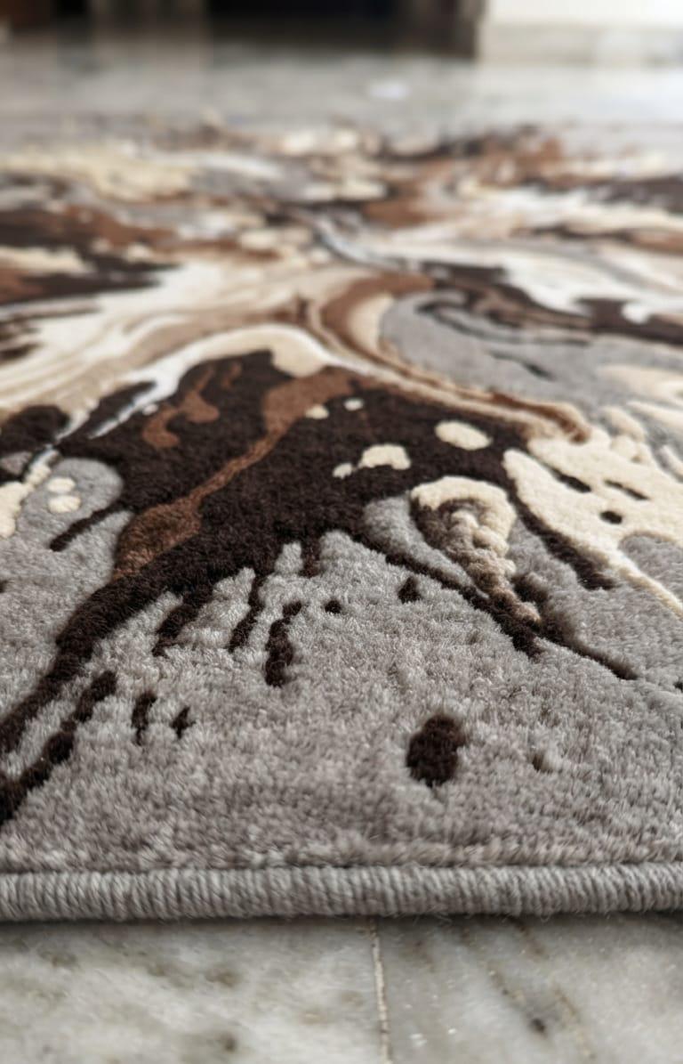 Detailed-hand-carved-3d-embossing-high-low-pile-texture-neutral-grey-mocha-brown-wool-rug  A close-up of a textured area rug with an abstract marbled pattern in shades of brown, beige, and gray, resting on a light marble floor.