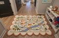 Muted pastel children road map playroom area rug styled on a dark wood floor inside a modern contemporary luxury Montessori nursery room
 A large children's play rug featuring a whimsical road trip scene with houses, trees, cars, and a bridge, laid out on a light wood floor in a hallway.