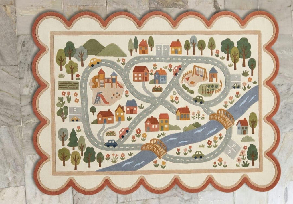 Shubham Art Rugs hand tufted New Zealand wool kids road map play rug featuring an ivory cream base with a unique scalloped border layout
 A rectangular children's play rug with a scalloped border, featuring a whimsical village scene with winding roads, houses, trees, cars, and a blue river on a light beige background.